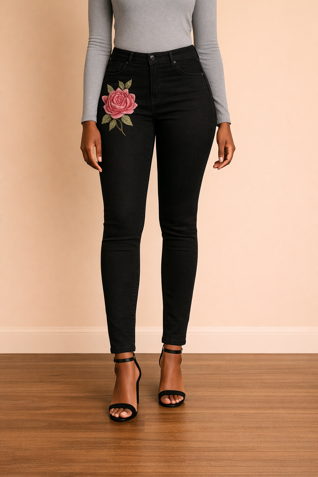 Pantalón Cashia Toledo negro en medio plano inferior, con bordado floral lateral y corte ajustado sobre fondo nude y suelo de madera.