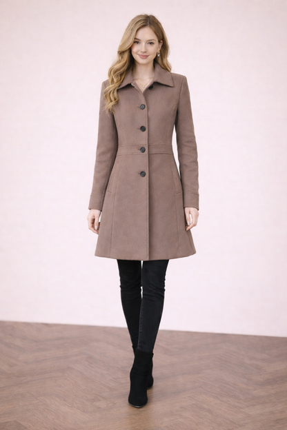 Abrigo Cashia Berlín color coffee brown de algodón, frontal cuerpo entero abotonado, modelo femenina sobre fondo nude con suelo parquet marrón, estilo elegante y ajuste entallado.