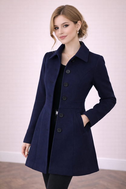Abrigo Cashia Berlín color azul marino de algodón con cinco botones frontales, corte entallado y largo medio, modelo femenina sobre fondo nude con suelo parquet marrón, estilo elegante y premium
