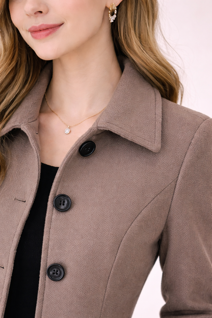 Detalle de cuello y botones del abrigo Cashia Berlín color coffee brown de algodón, tejido texturizado y corte entallado, fondo nude con estilo elegante y premium.