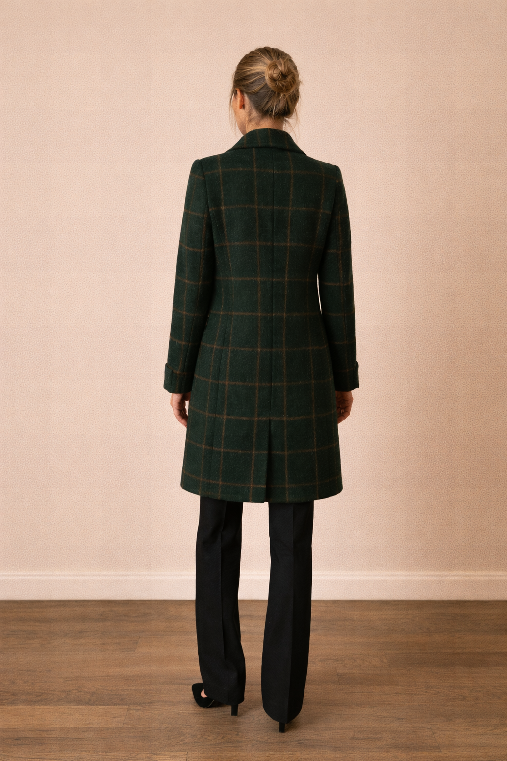 Abrigo Cashia Copenhague verde oscuro de cuadros en vista trasera de cuerpo entero, corte recto y largo a la rodilla, sobre fondo nude liso con suelo de parquet marrón oscuro.