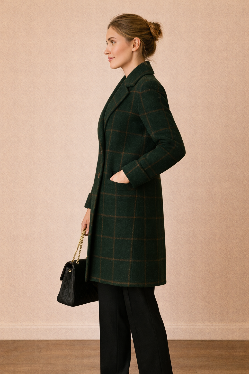 Abrigo Cashia Copenhague verde oscuro de cuadros en vista de perfil, corte recto y largo a la rodilla, con cierre frontal de dos botones en línea vertical, sobre fondo nude con suelo de madera.