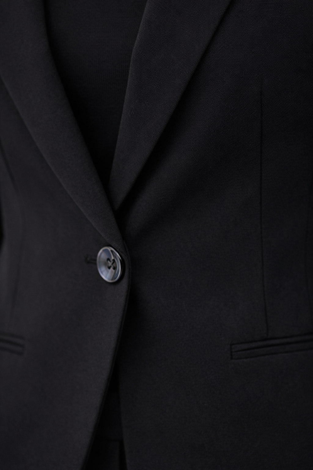 Detalle del botón frontal y solapa del blazer Cashia Helena en color negro con bolsillo vivo sin solapa y tejido liso estructurado.