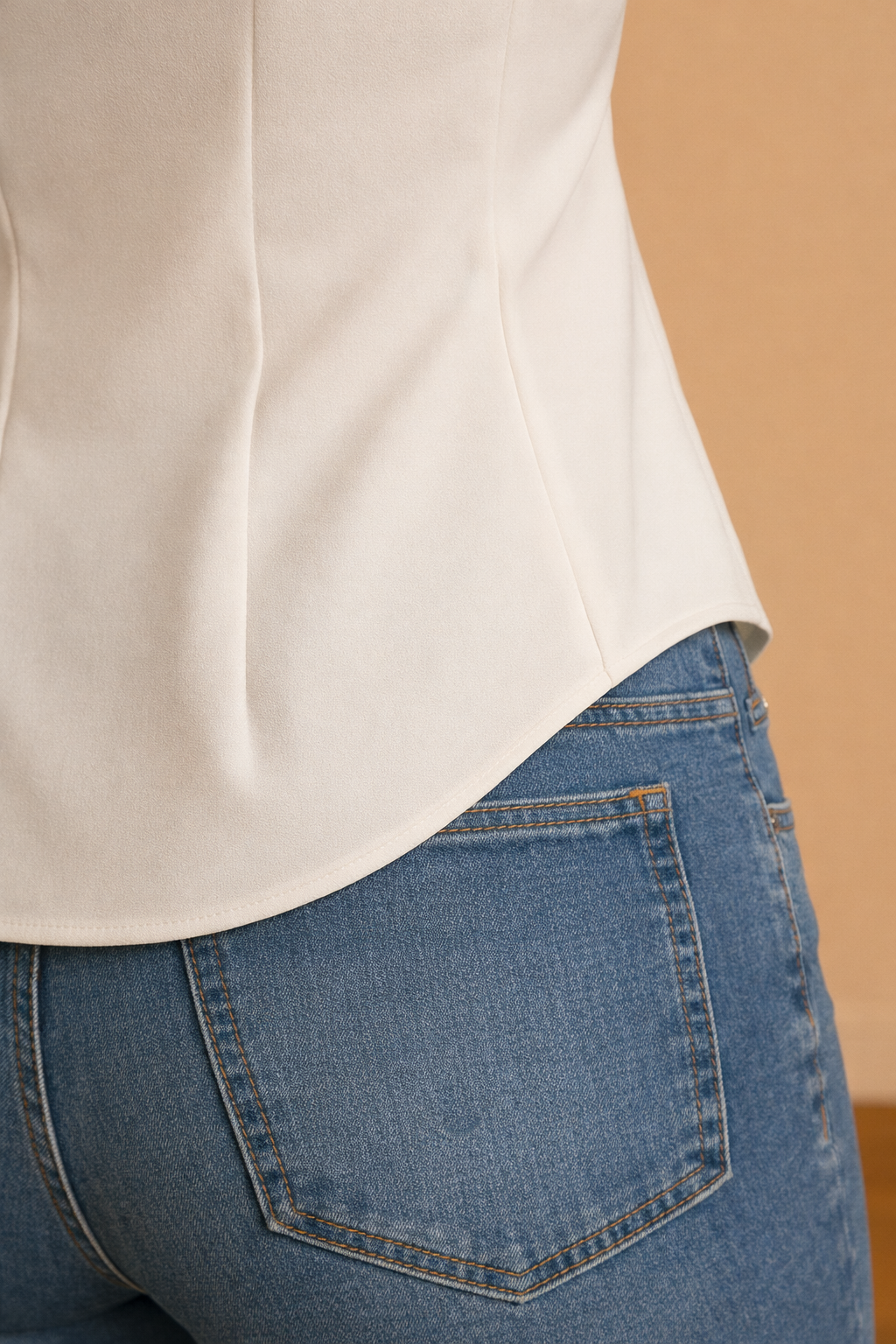 Detalle del bajo curvo de la camisa Cashia Cartagena blanca, acabado limpio y costura fina, fondo nude con suelo de parquet marrón.