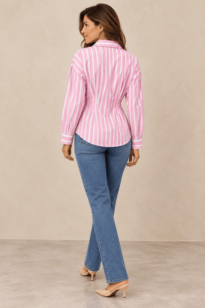 Modelo morena de espalda con Camisa Cashia Clara de rayas rosas y blancas, manga larga y cintura entallada.