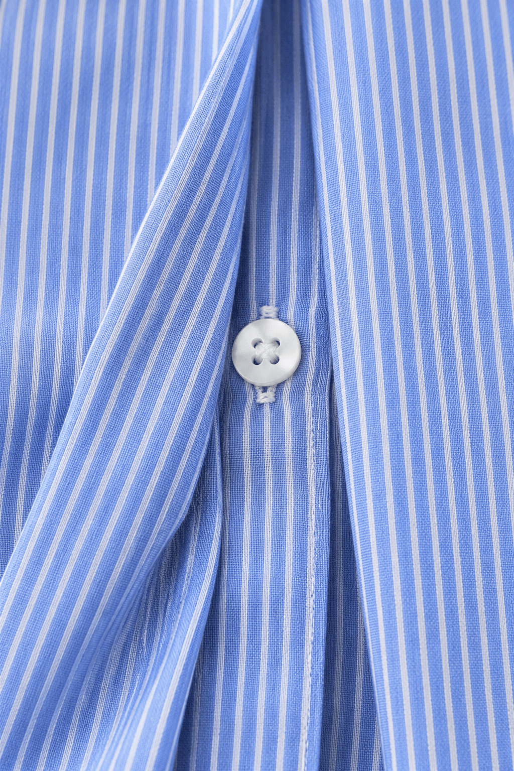 Detalle de la tapeta ligeramente apartada de la camisa Cashia Elisa azul, mostrando el botón blanco del cierre oculto.