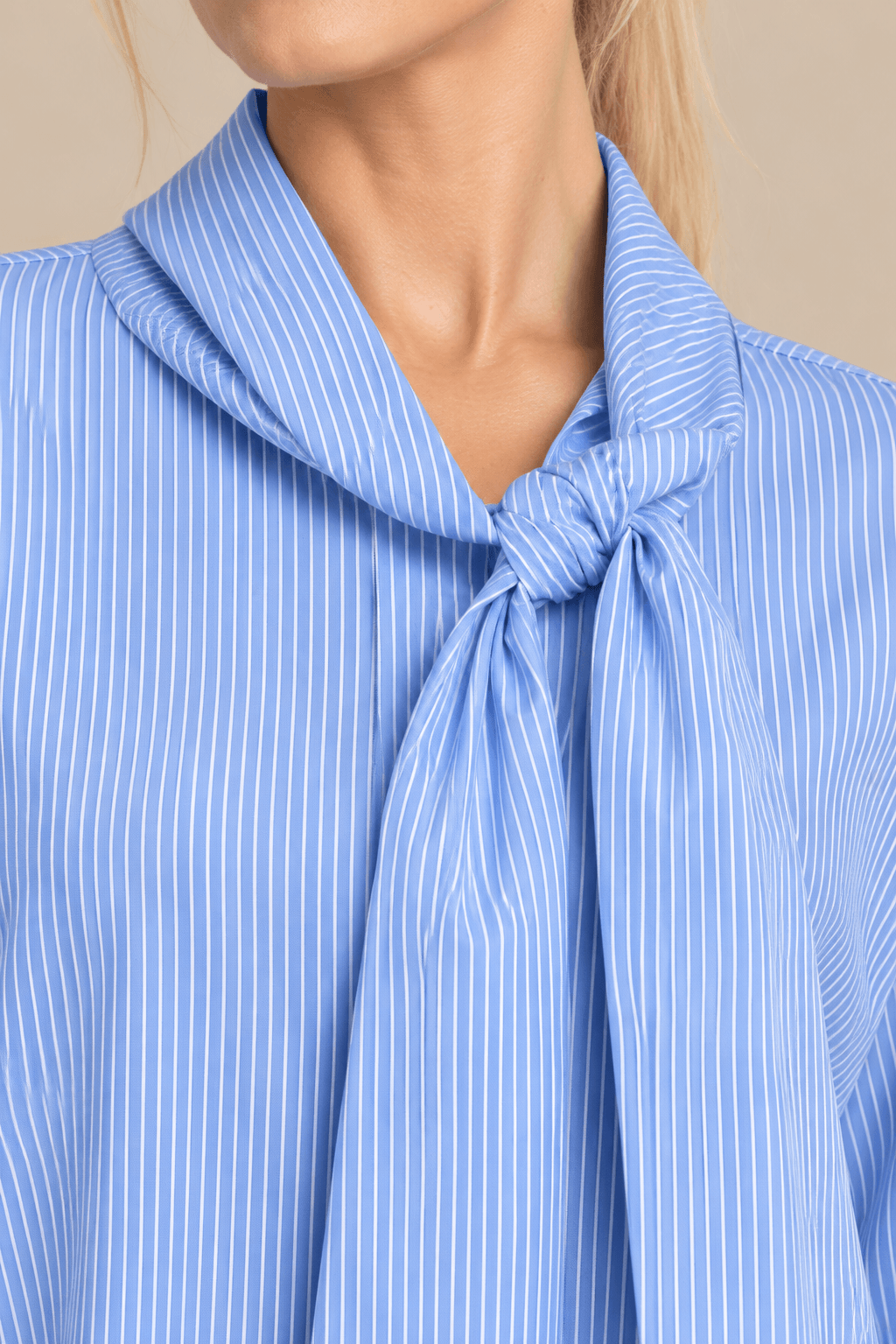 Primer plano del cuello con lazada anudada de la camisa Cashia Elisa azul, mostrando las rayas finas y el acabado del tejido.