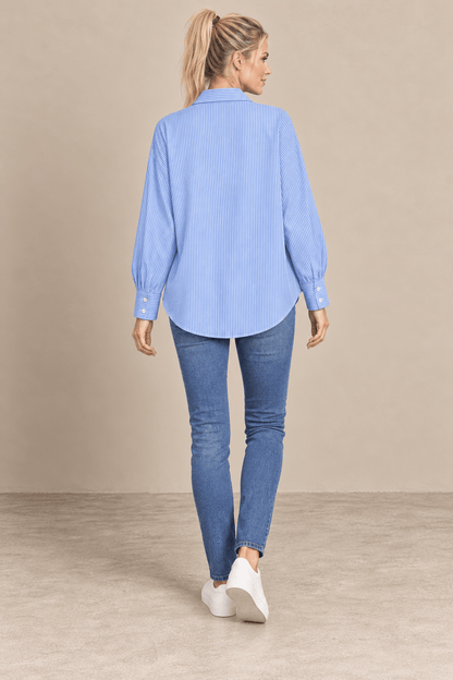 Camisa Cashia Elisa azul vista de espalda, con rayas verticales finas y bajo redondeado, combinada con vaqueros.