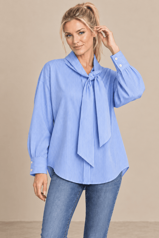 Modelo rubia con camisa Cashia Elisa azul en medio plano superior, mostrando la lazada y el puño con dos botones blancos.