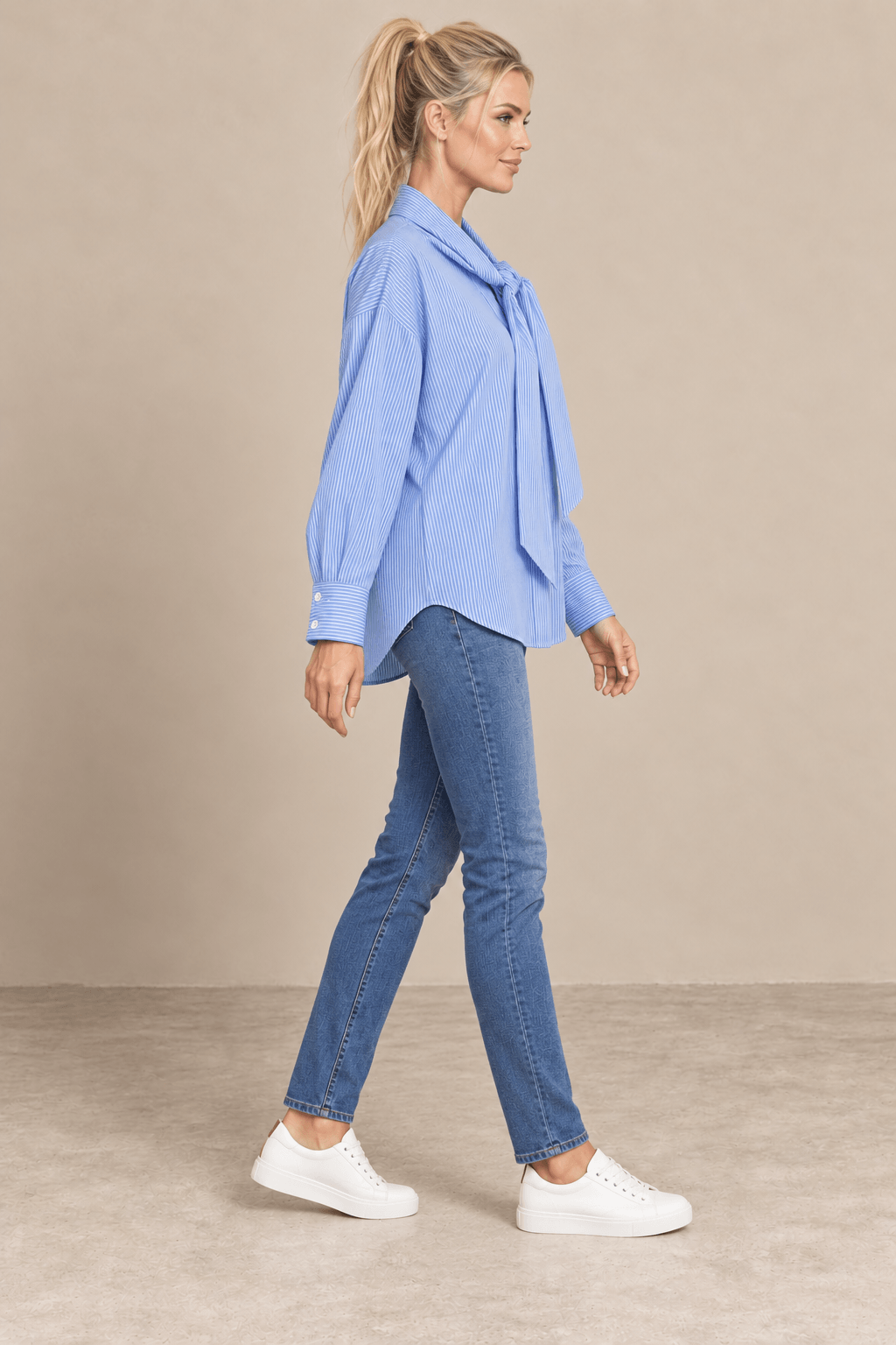Vista de perfil derecho de la camisa Cashia Elisa azul, con manga larga, puños anchos y bajo curvo sobre vaqueros.