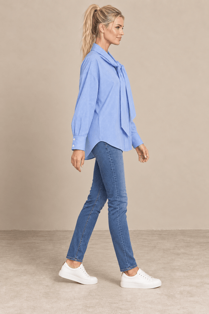 Vista de perfil derecho de la camisa Cashia Elisa azul, con manga larga, puños anchos y bajo curvo sobre vaqueros.