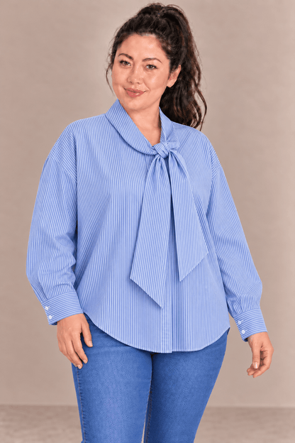 Camisa Cashia Elisa azul en talla L, sobre modelo asiática con cola alta, en medio plano superior y combinada con vaqueros.