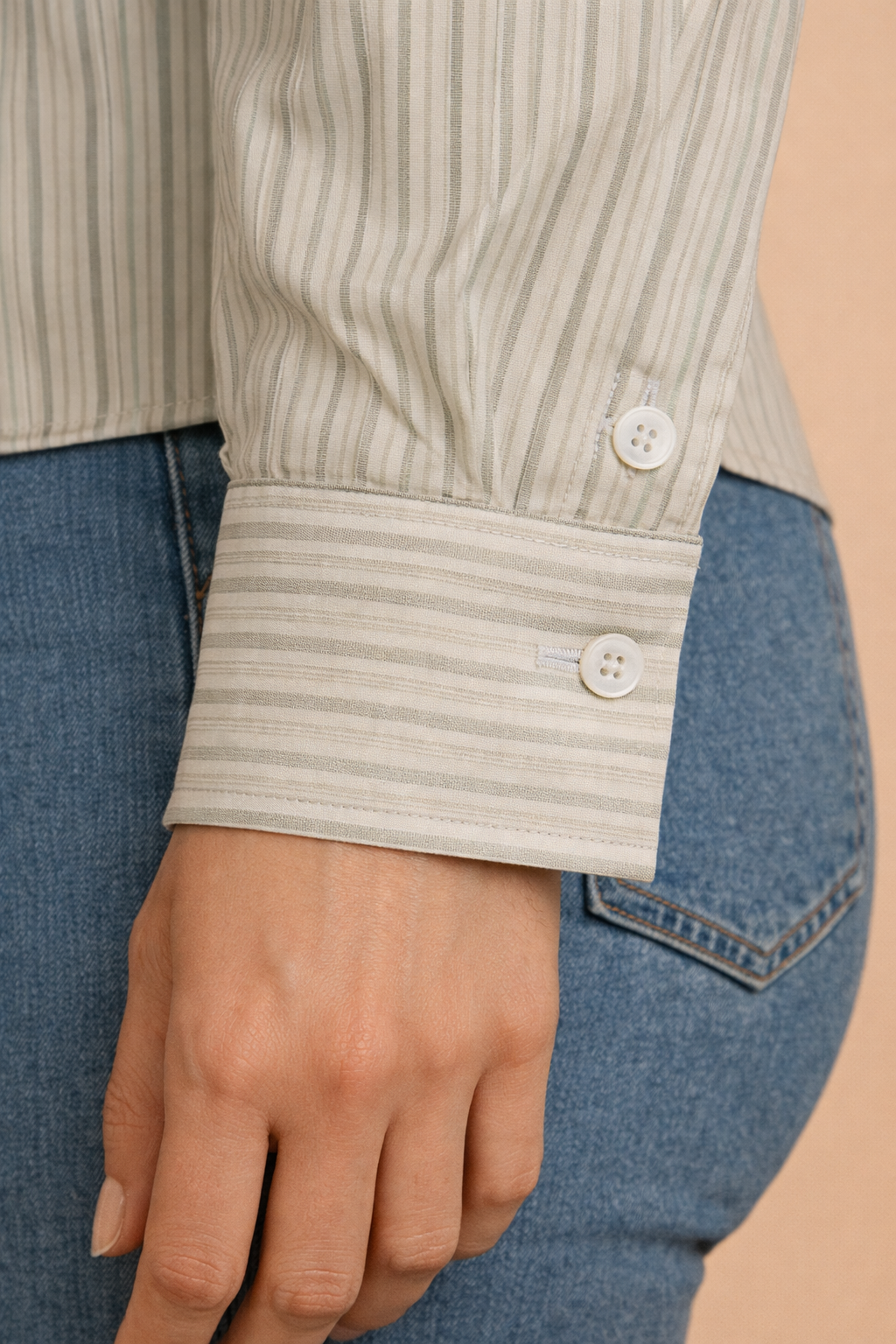 Detalle de la manga de la camisa Cashia en tono beige con rayas verticales, puño abotonado y acabado clásico, fondo nude.
