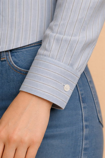 Detalle del puño de la camisa Cashia en tono azul claro con rayas verticales, puño abotonado y acabado clásico, fondo nude.