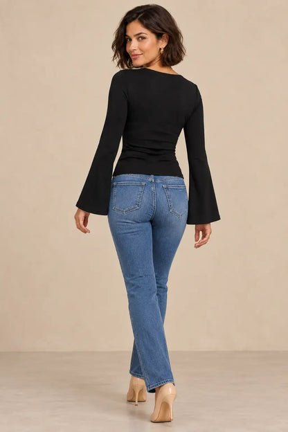 Mujer usando camiseta escote cruzado mangas acampanadas, vista trasera, con jeans ajustados.