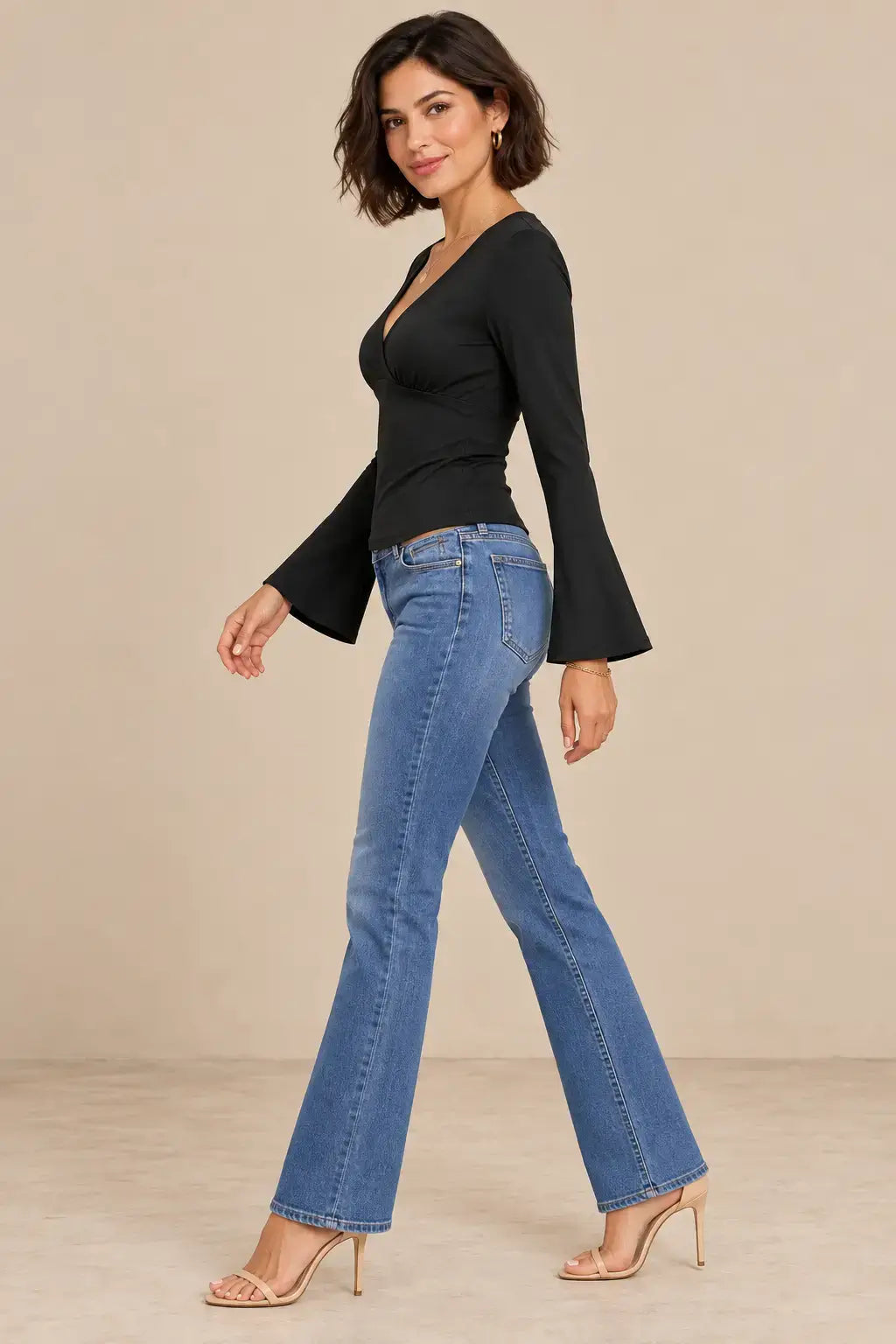 Mujer luciendo una camiseta escote cruzado mangas acampanadas con jeans en un fondo neutro.
