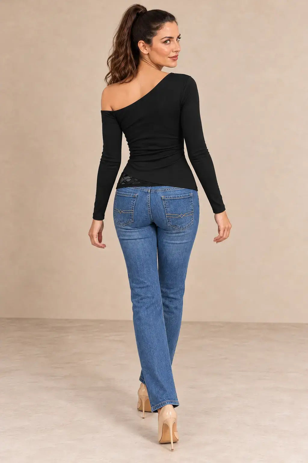Mujer de espaldas con camiseta negra manga larga encaje asimétrico y jeans claros, mostrando estilo moderno.