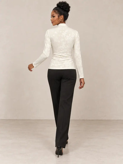 Mujer de espaldas vistiendo camiseta mujer cuello mao detalle floral en color blanco y pantalones negros.