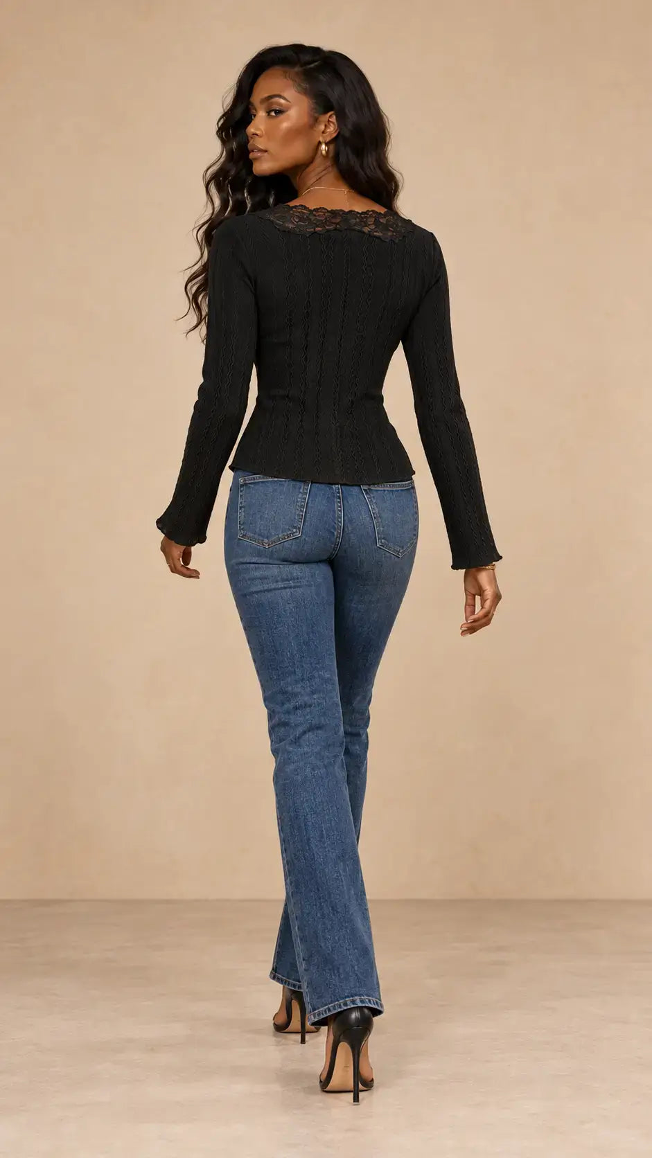Mujer con camiseta larga encaje botones negra y jeans azules de espaldas, luciendo elegante y moderna.