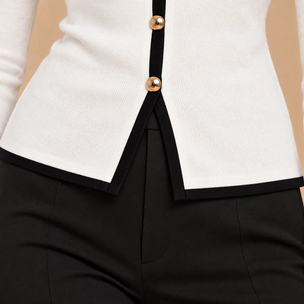 cardigan-cashia-irati-blanco-detalle-abertura-bajo.png	Detalle de la abertura delantera del bajo con ribete negro del cárdigan Cashia Irati blanco.