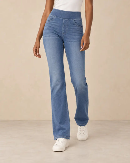 Pantalón Cashia Denim 200 en denim medio, medio plano inferior sobre modelo talla S de raza negra, con camiseta blanca de manga corta y zapatillas blancas, en pose natural sobre fondo beige.