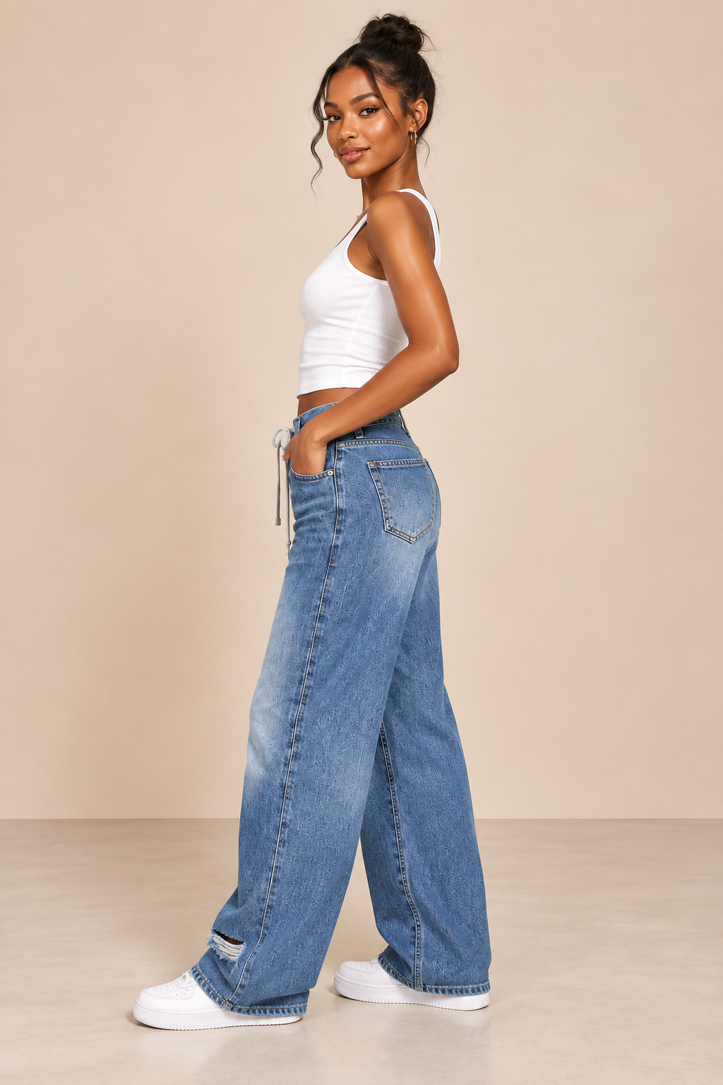 Pantalón Cashia Denim 303 en azul denim claro con cordón en cintura y bajo roto, vista de perfil con modelo S y camiseta blanca de tirantes.
