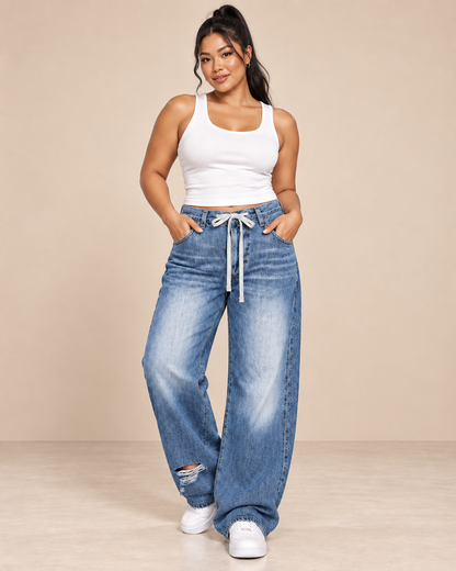 Pantalón Cashia Denim 303 en azul denim claro con cordón en cintura y bajo roto, imagen de cuerpo entero en talla L con camiseta blanca de tirantes y deportivas blancas.