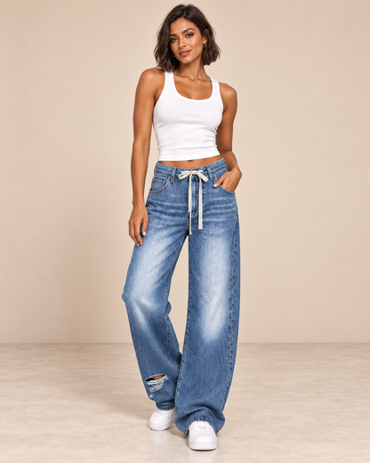 Pantalón Cashia Denim 303 en azul denim claro con cordón en cintura y bajo roto, imagen de cuerpo entero en talla M con camiseta blanca de tirantes y deportivas blancas.