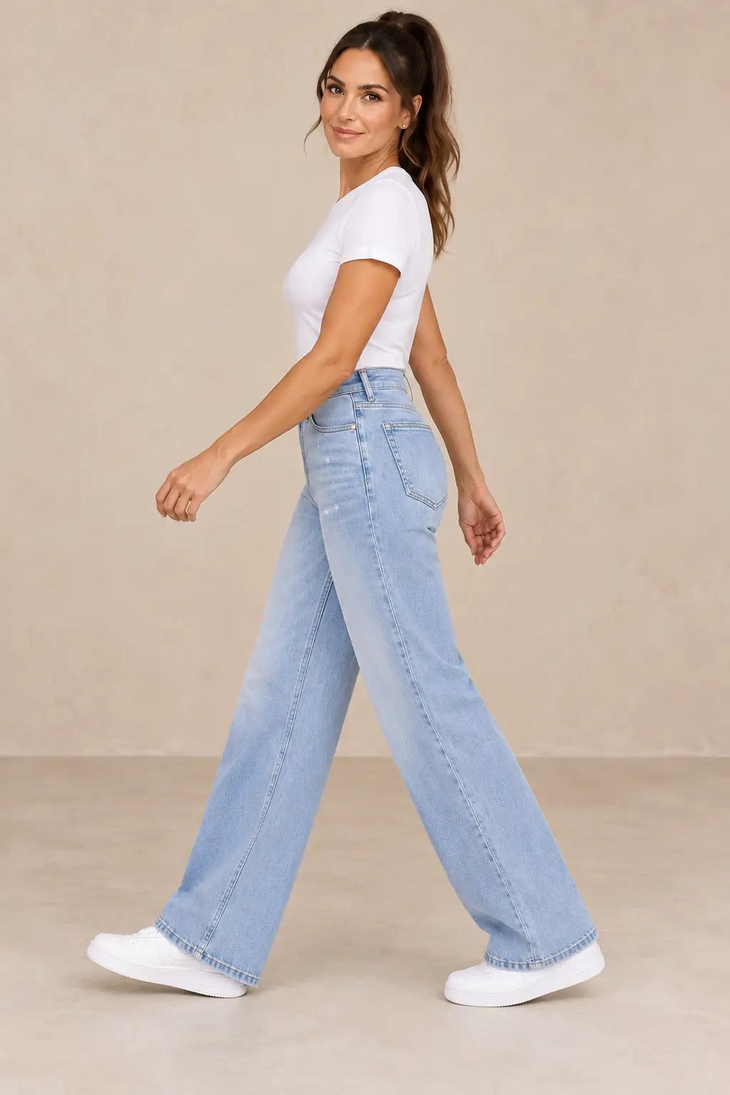 Vista lateral del pantalón Cashia Denim 402 azul claro con modelo caminando y coleta alta.