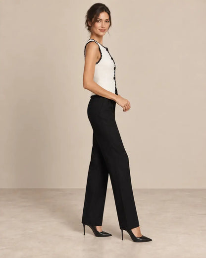 Chaleco Cashia Elegance blanco con ribete negro en talla S, sobre modelo Cashia morena elegante con pelo semirecogido, pantalón de vestir negro y tacones negros, vista lateral derecha de cuerpo entero.