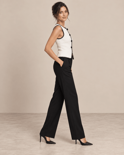 Chaleco Cashia Elegance blanco con ribete negro en talla S, sobre modelo Cashia morena elegante y maquillada con pelo semirecogido, pantalón de vestir negro y tacones negros, vista lateral izquierda de cuerpo entero.