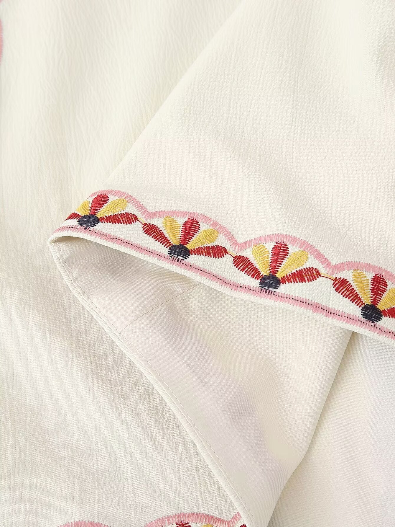Detalle del bajo con bordado decorativo en el Chaleco Cashia Nice crema con acabado ondulado en tonos rosa, amarillo y negro