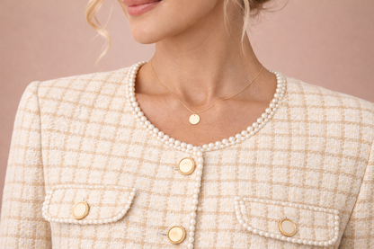 Detalle del cuello redondo de la chaqueta Cashia Capri en tejido tweed beige con acabado de perlitas en el filo, mostrando botones planos dorados y textura estructurada del tejido.