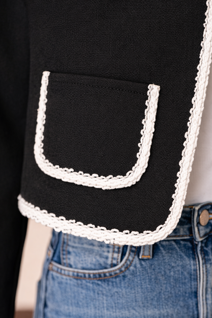 Detalle del bolsillo inferior con ribete blanco de la chaqueta corta Cashia Lady en color negro con tejido texturizado.
