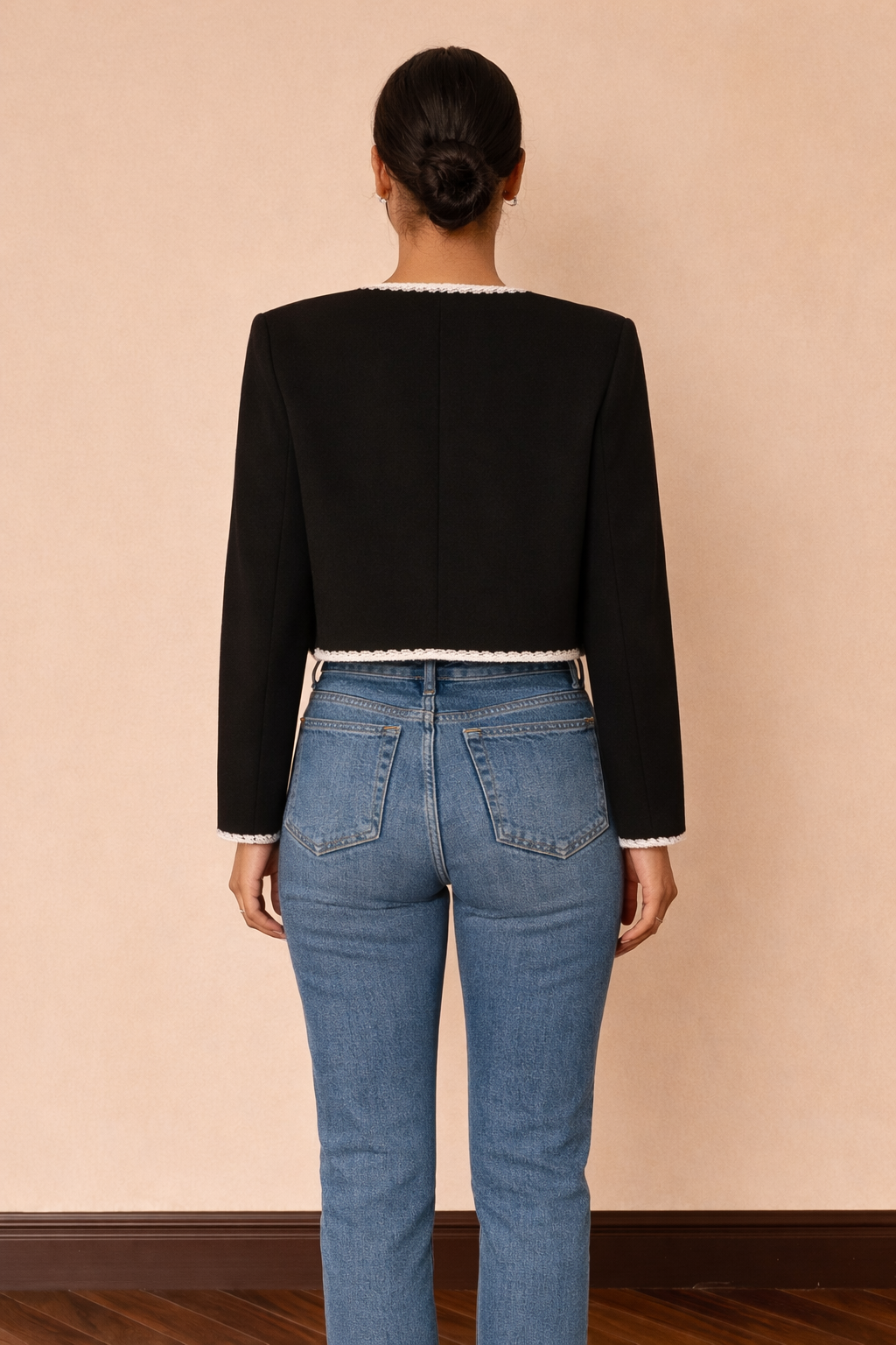 Chaqueta corta Cashia Lady en color negro con ribetes blancos, vista trasera de cuerpo entero combinada con top blanco y jeans azul de tiro alto.