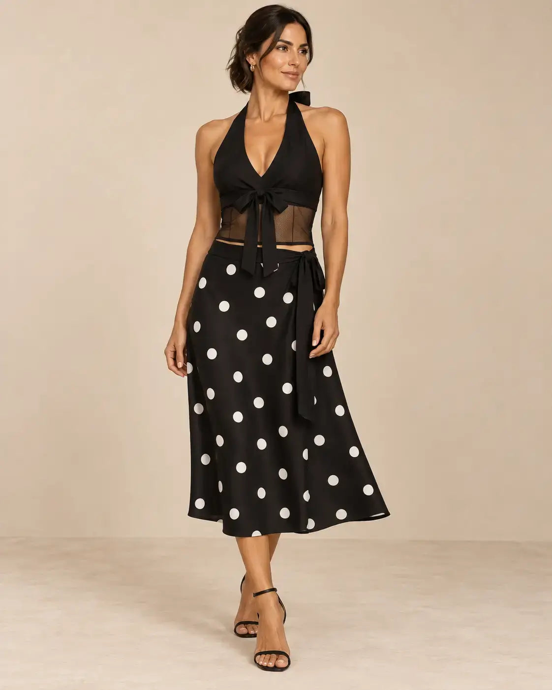Conjunto Cashia Livorno negro de dos piezas en modelo talla M, top halter con lazada y transparencias y falda midi de lunares blancos.