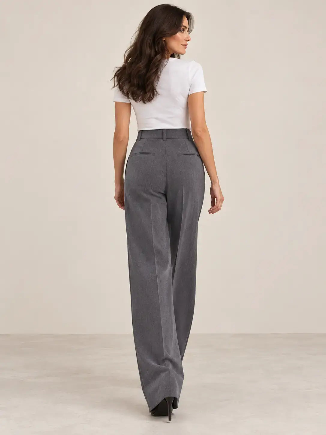Mujer usando pantalón de mujer tiro alto pinzas con pierna amplia en color gris, vista trasera.