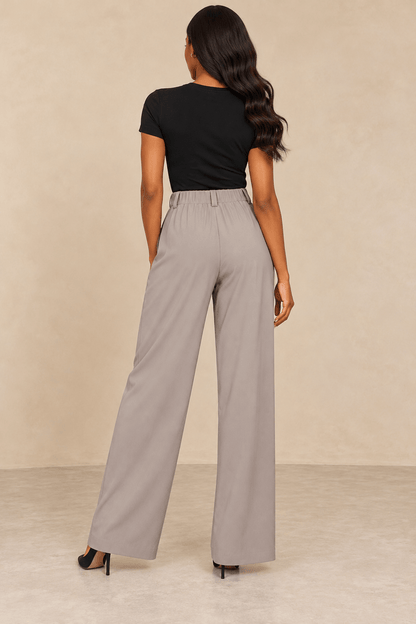 Mujer usando pantalón ancho tiro alto gris claro, visto desde atrás, con blusa negra.