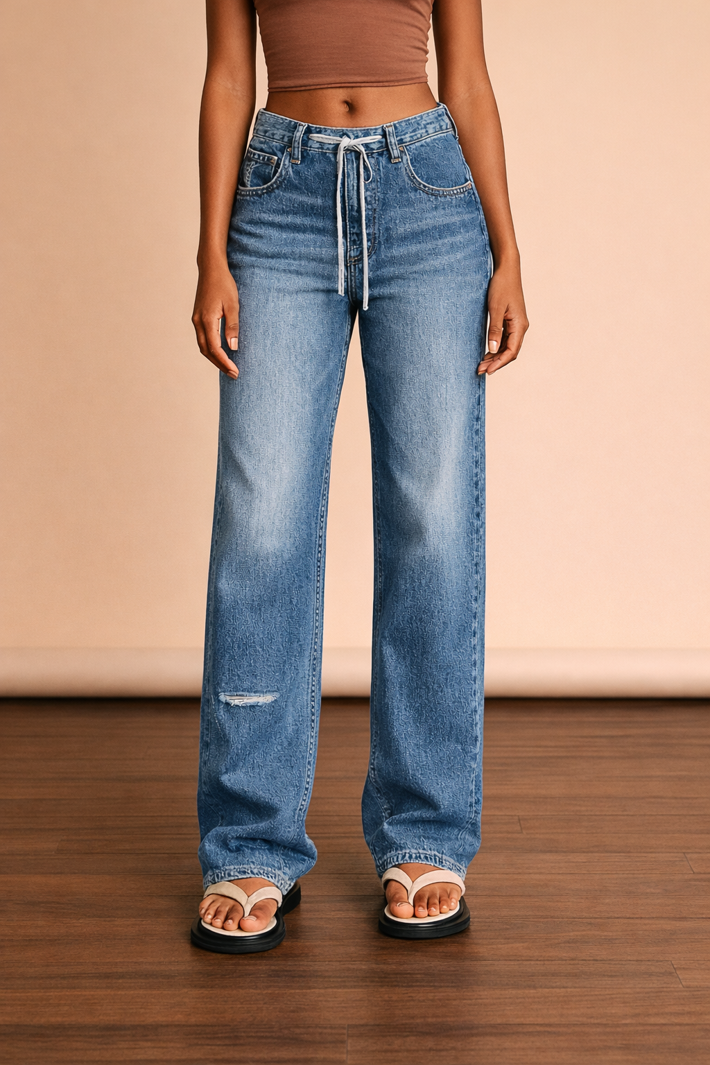 Pantalón Cashia Barcelona vaquero de pierna ancha en medio plano inferior de cintura a talón, con cinturilla ajustable y bajo amplio sobre fondo nude y suelo de madera.