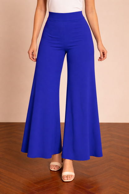 Pantalón Cashia Granada azul en medio plano inferior, con cintura alta y pierna ancha de caída fluida hasta el bajo, sobre fondo nude y suelo de madera en espiga.