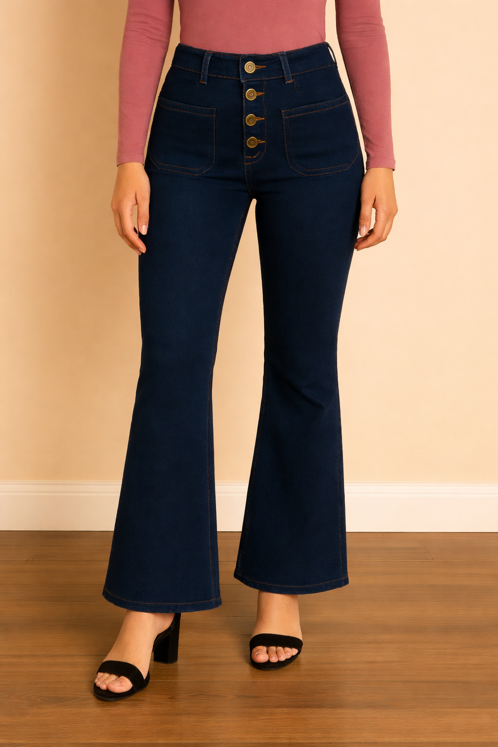 Pantalón Cashia Málaga azul denim oscuro en plano medio inferior, de cintura a tacón, con tiro alto, cierre frontal de botones y corte acampanado, sobre fondo nude con suelo de parquet marrón oscuro.
