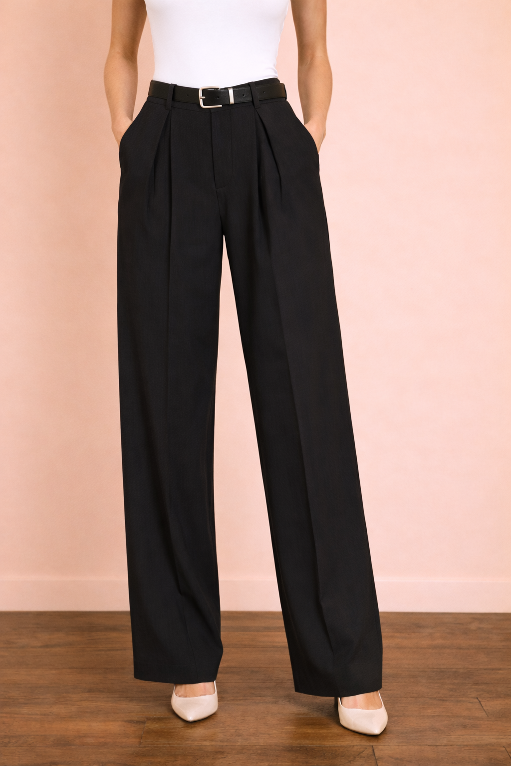 Pantalón Cashia Sevilla en tono negro en plano medio inferior, de cintura a tacón, con tiro alto, pinzas delanteras y pernera ancha de caída fluida, sobre fondo nude con suelo de parquet marrón oscuro.