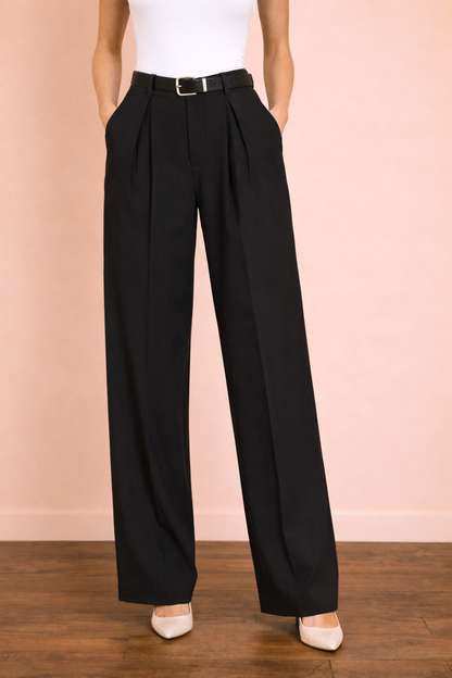 Pantalón Cashia Sevilla en tono negro en plano medio inferior, de cintura a tacón, con tiro alto, pinzas delanteras y pernera ancha de caída fluida, sobre fondo nude con suelo de parquet marrón oscuro.