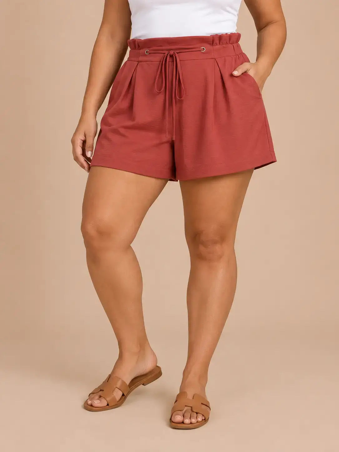 Short Cashia Arezzo teja en talla L, con cintura fruncida, cordón ajustable y pernera amplia, en medio plano inferior con una pierna flexionada.