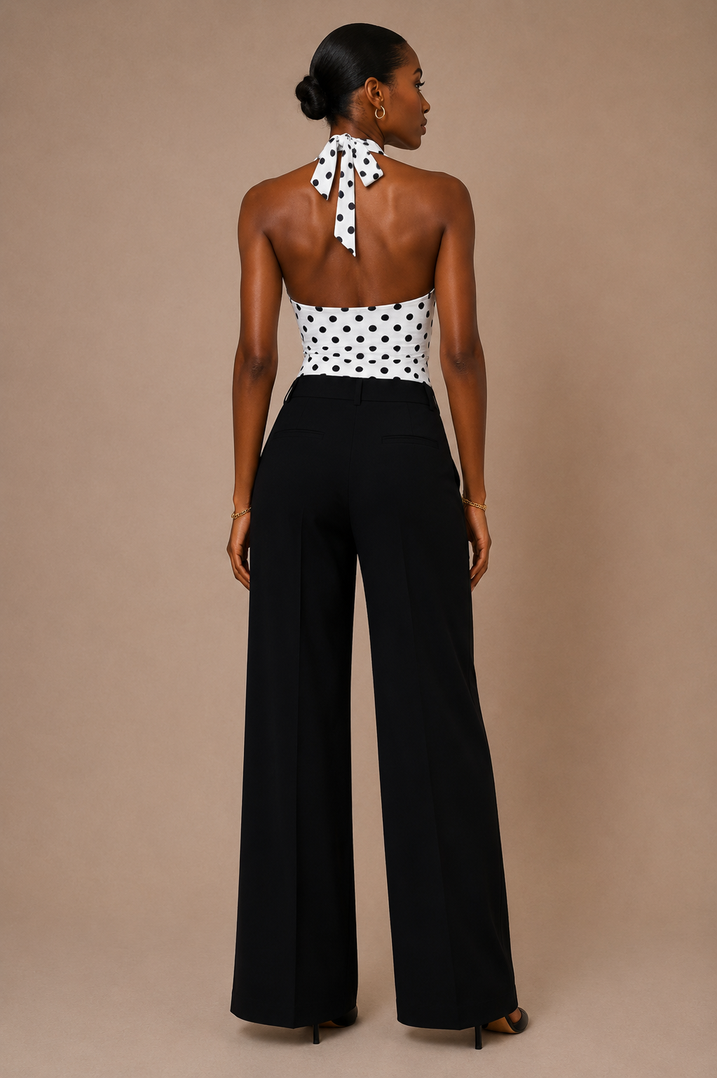 Vista de espalda del Top Cashia Amalfi blanco de lunares, con cuello halter anudado y pantalón negro sobre fondo nude.