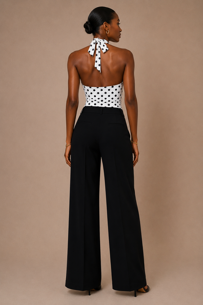 Vista de espalda del Top Cashia Amalfi blanco de lunares, con cuello halter anudado y pantalón negro sobre fondo nude.