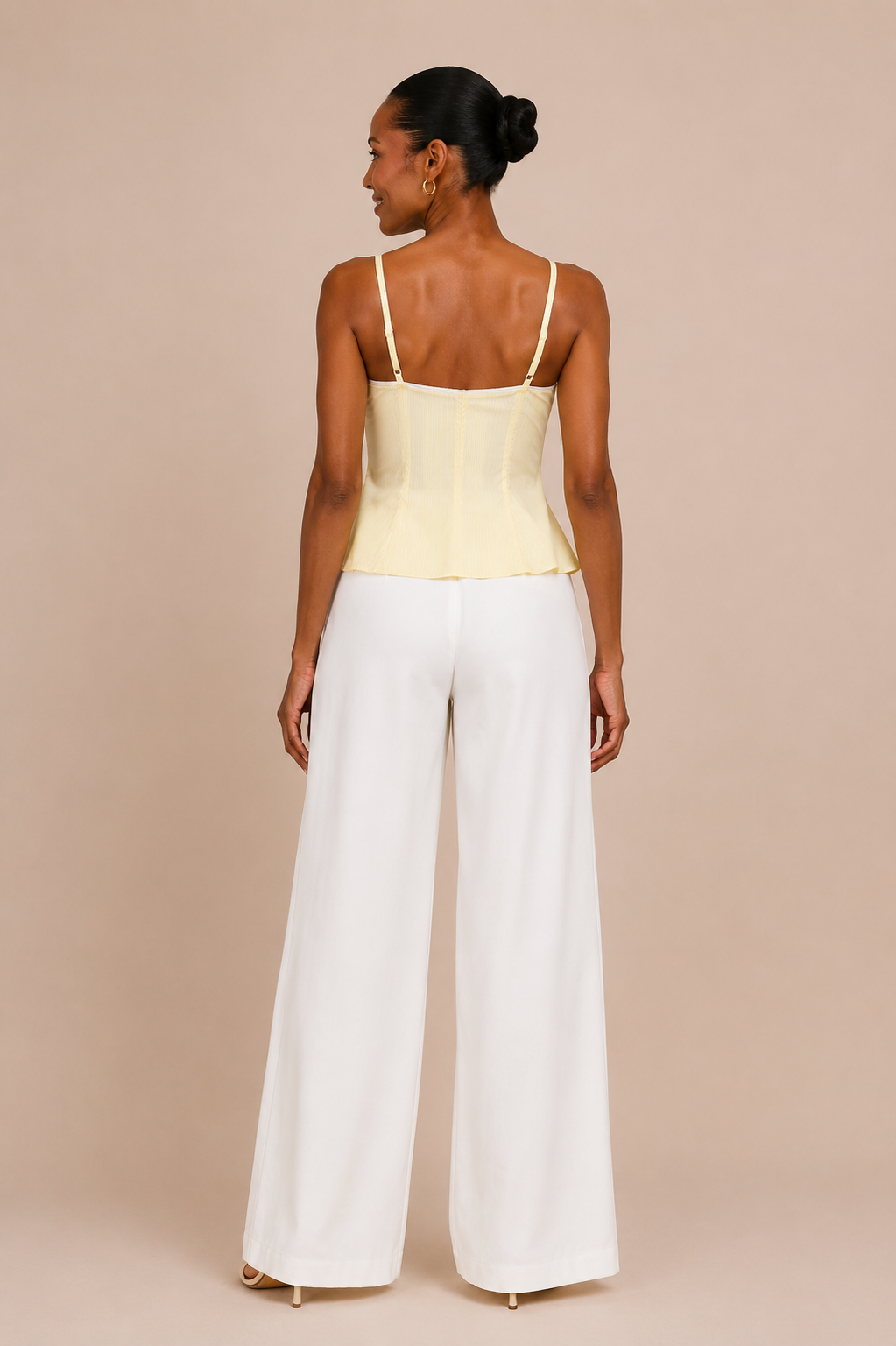Vista de espalda del Top Cashia Bari amarillo con tirantes finos y pantalón blanco wide leg sobre fondo nude.