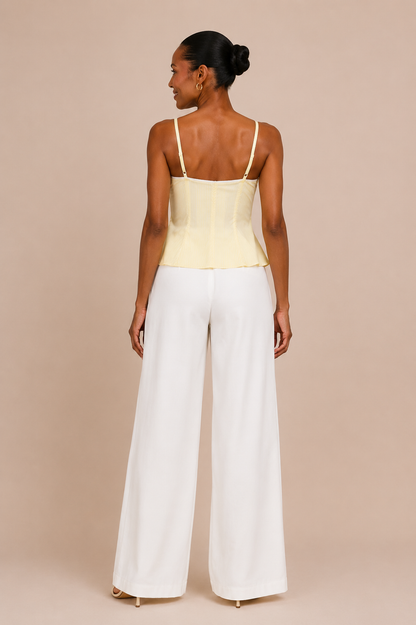 Vista de espalda del Top Cashia Bari amarillo con tirantes finos y pantalón blanco wide leg sobre fondo nude.