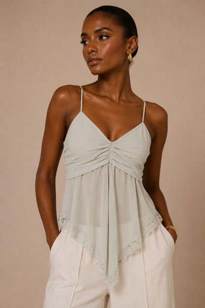 Modelo Cashia de raza negra con Top Cashia Lucca gris claro de tirantes finos, frunce frontal y bajo con encaje, combinado con pantalón blanco sobre fondo nude.