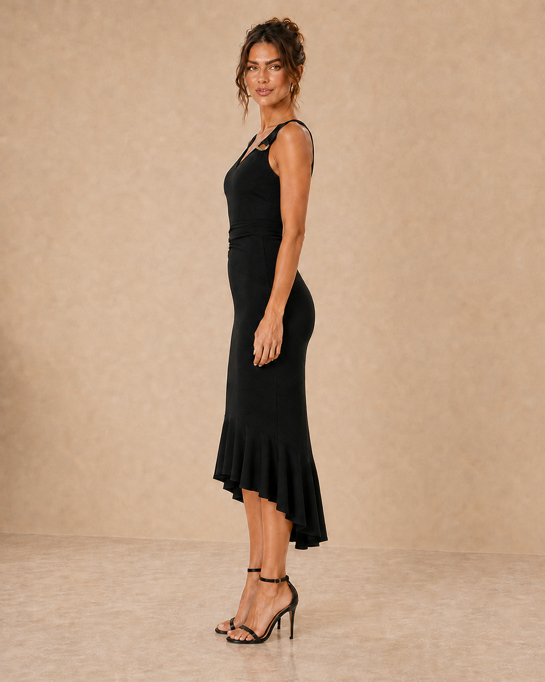 Vestido Cashia Marbella negro visto de perfil, con bajo asimétrico, volante continuo y hebillas doradas.